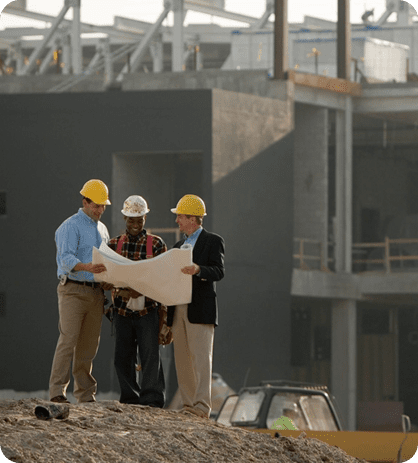 Three men in hard hats and one is holding a plan