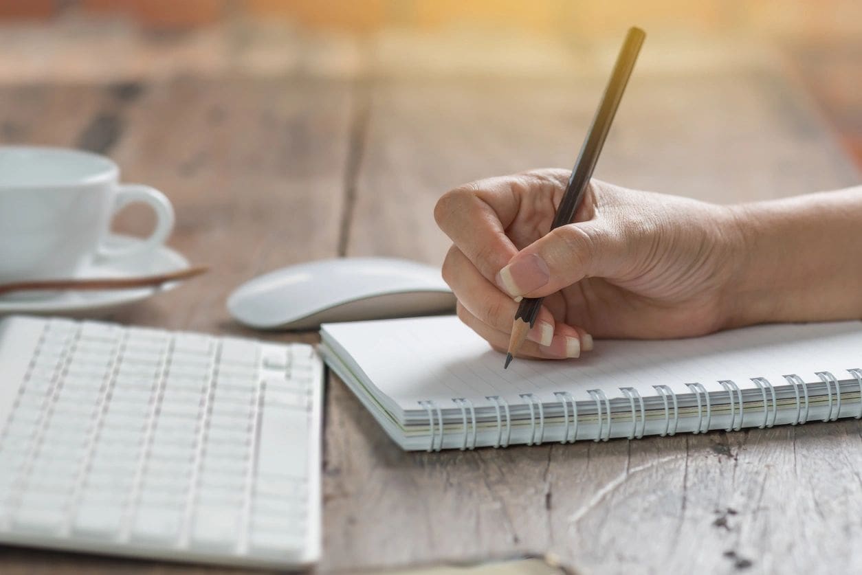 A person writing in a notebook on top of a table.